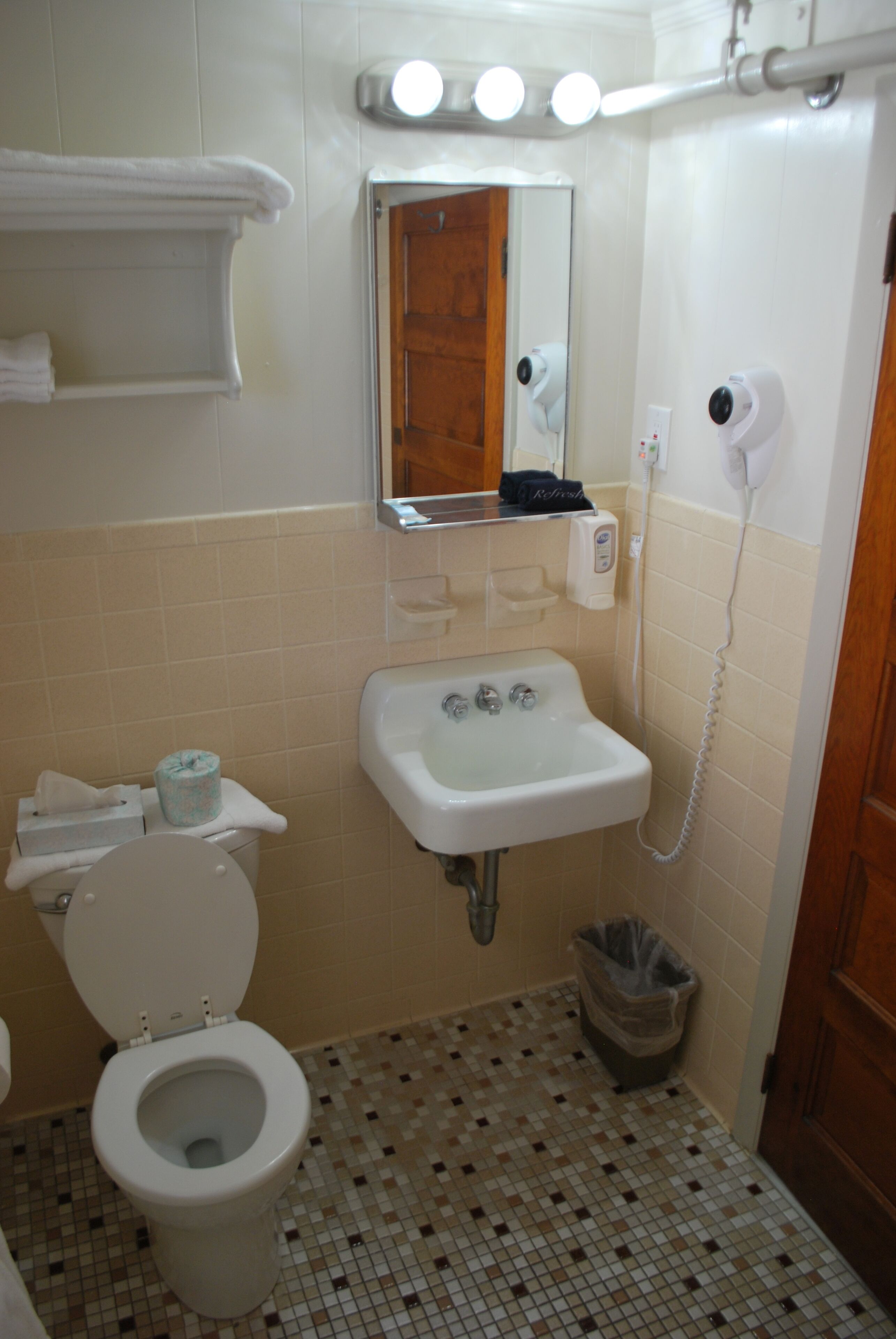 Un baño con inodoro, lavabo, espejo, toallero y un cubo de basura.
