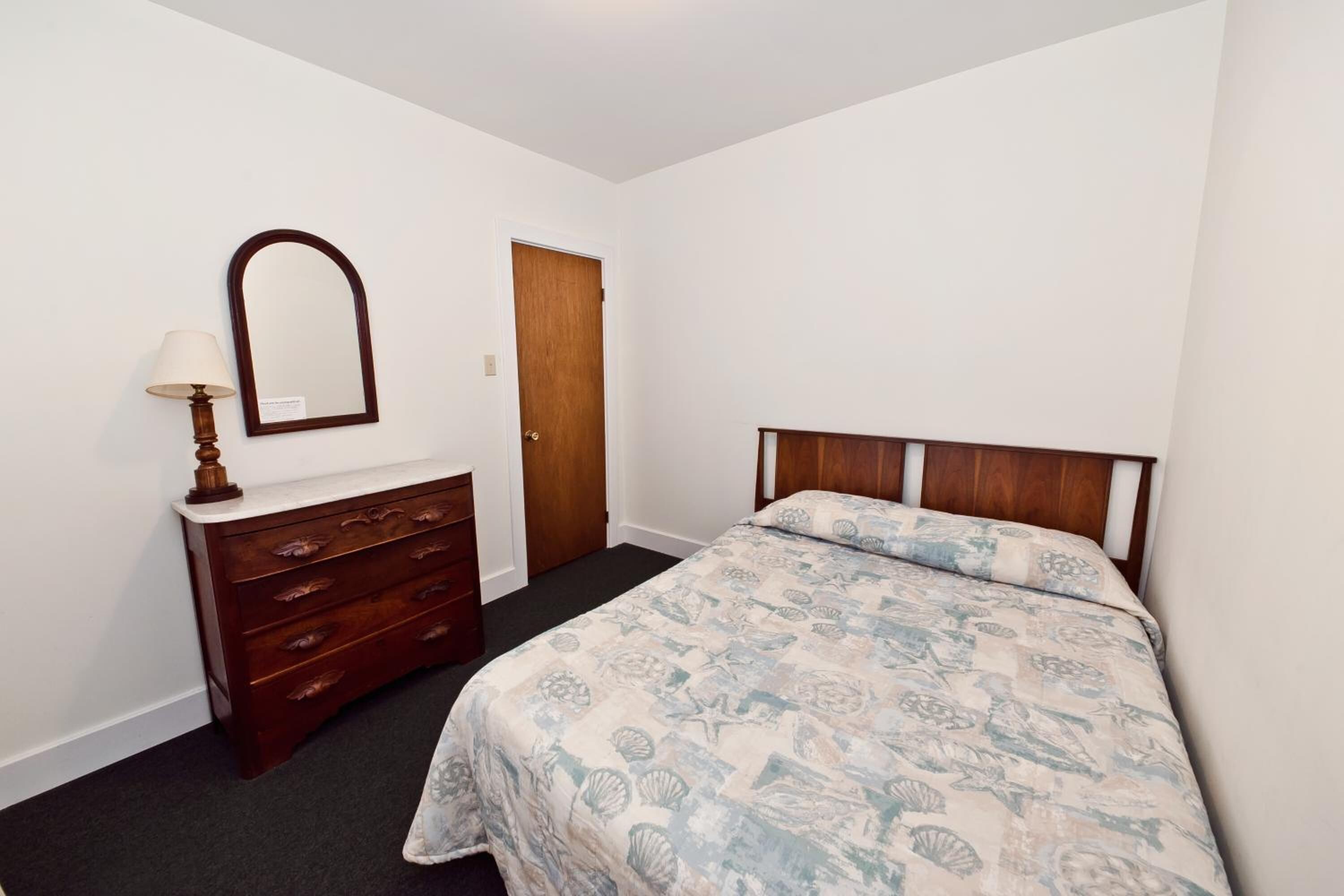 A bedroom with a bed, a dresser, a mirror, and a door.