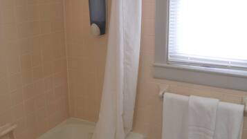 A bathroom with a bathtub, a shower curtain, a window, and a tiled floor.