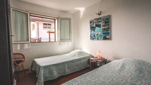 Una habitación con dos camas individuales, un ventanal con vistas, una silla de mimbre y un cuadro de temática náutica en la pared.
