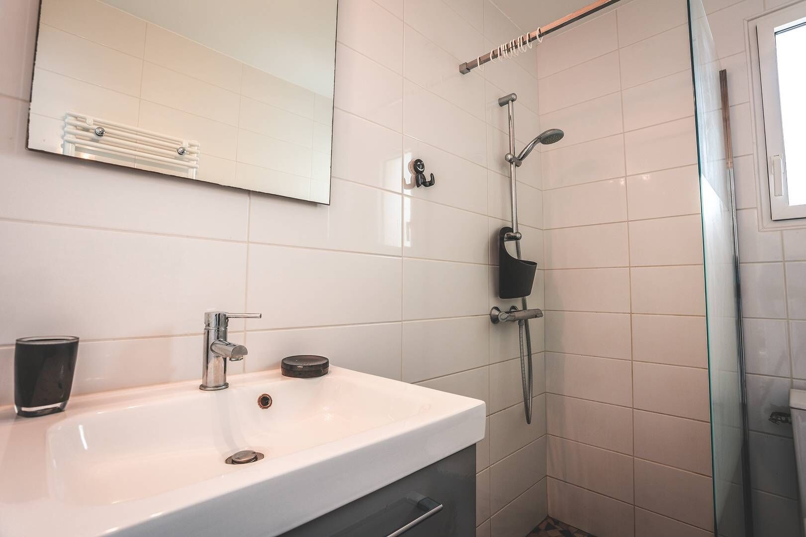 Une salle de bain avec un lavabo blanc, un miroir, une douchette à main et une paroi de douche en verre.