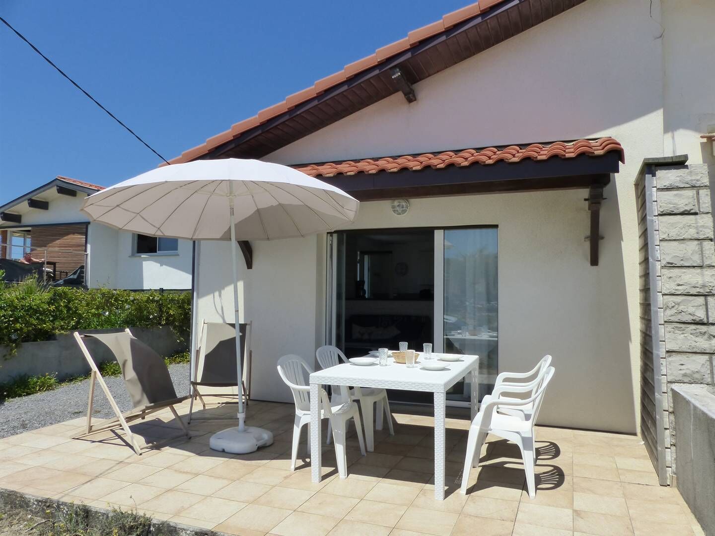 An outdoor patio with a table and chairs, a white umbrella, and a sliding glass door.