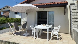 Un patio al aire libre con una mesa y sillas, un paraguas blanco y una puerta corrediza de vidrio.