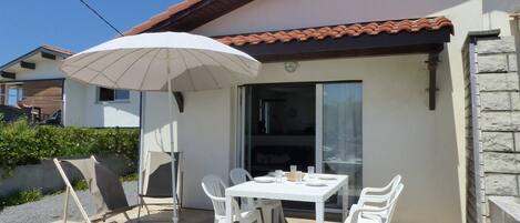 An outdoor patio with a table and chairs, a white umbrella, and a sliding glass door.