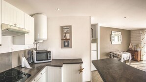 Una cocina con armarios blancos, un microondas y una estufa. Hay una zona de comedor con una mesa y sillas, y un televisor sobre un mueble de madera.