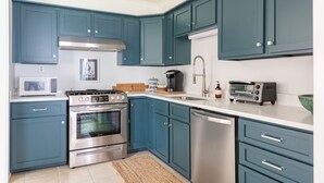 A modern kitchen with teal cabinets, stainless steel appliances, and a white countertop. - Palmetto Cottage - Historic 1925 cottage in Downtown Fairhope (Fairhope)