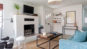 A modern living room with a fireplace, a television, and a coffee table. - Palmetto Cottage - Historic 1925 cottage in Downtown Fairhope (Fairhope)