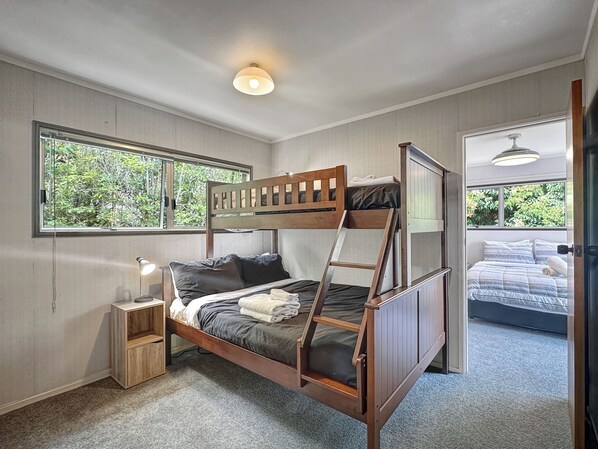 A bunk bed room with a window, a bedside table, and a lamp.