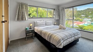 A bedroom with a large window, a bed with a striped blanket, a bedside table with a lamp, and curtains. - Central Spacious Family House - Paihia House (Paihia)