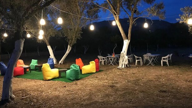 An outdoor seating area with colorful bean bags and tables under string lights, surrounded by trees. - Bodrum Masali Camping - Hostel (Bodrum)