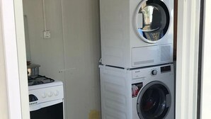 A compact laundry room with a stacked washer and dryer, a gas stove, and a small cabinet. - Bodrum Masali Camping - Hostel (Bodrum)