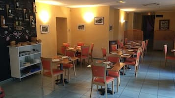 Un restaurant doté de plusieurs tables et chaises, d’un menu écrit à la craie et d’une étagère où sont exposés divers articles.