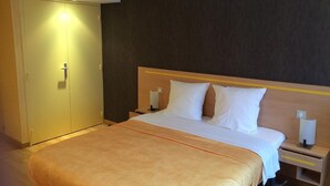 Een hotelkamer met een groot bed, een kledingkast, een nachtkastje en een wandlamp.