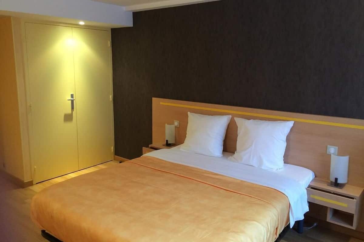 Una habitació d'hotel amb un llit gran, un armari, una tauleta de nit i una làmpada penjada a la paret.