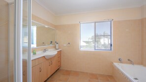A bathroom with a large mirror, two sinks, a bathtub, and a window with blinds.