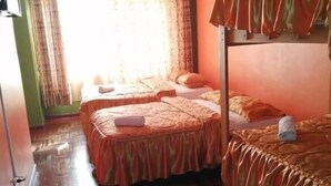 Ein Zimmer mit zwei Betten, Holzdielenboden und einem fenster mit Vorhängen.