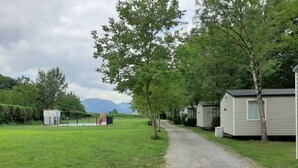 Uma trilha de cascalho conduz a casas móveis, com um campo gramado e árvores de ambos os lados.