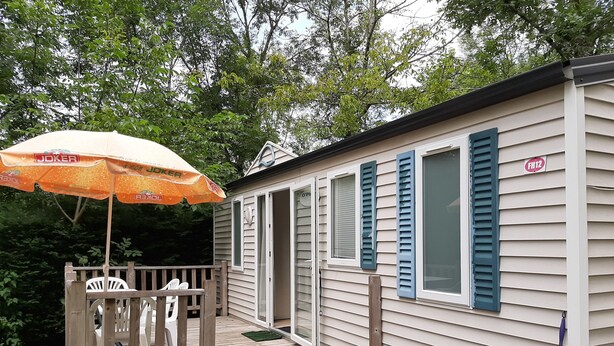 Uma casa móvel com um deck de madeira, área de estar ao ar livre e um guarda-sol.