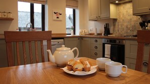 Una cocina con una mesa de madera, una tetera, magdalenas y dos tazas.
