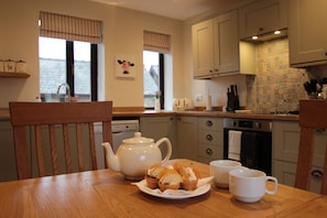 A kitchen with a wooden table, a teapot, muffins, and two mugs.