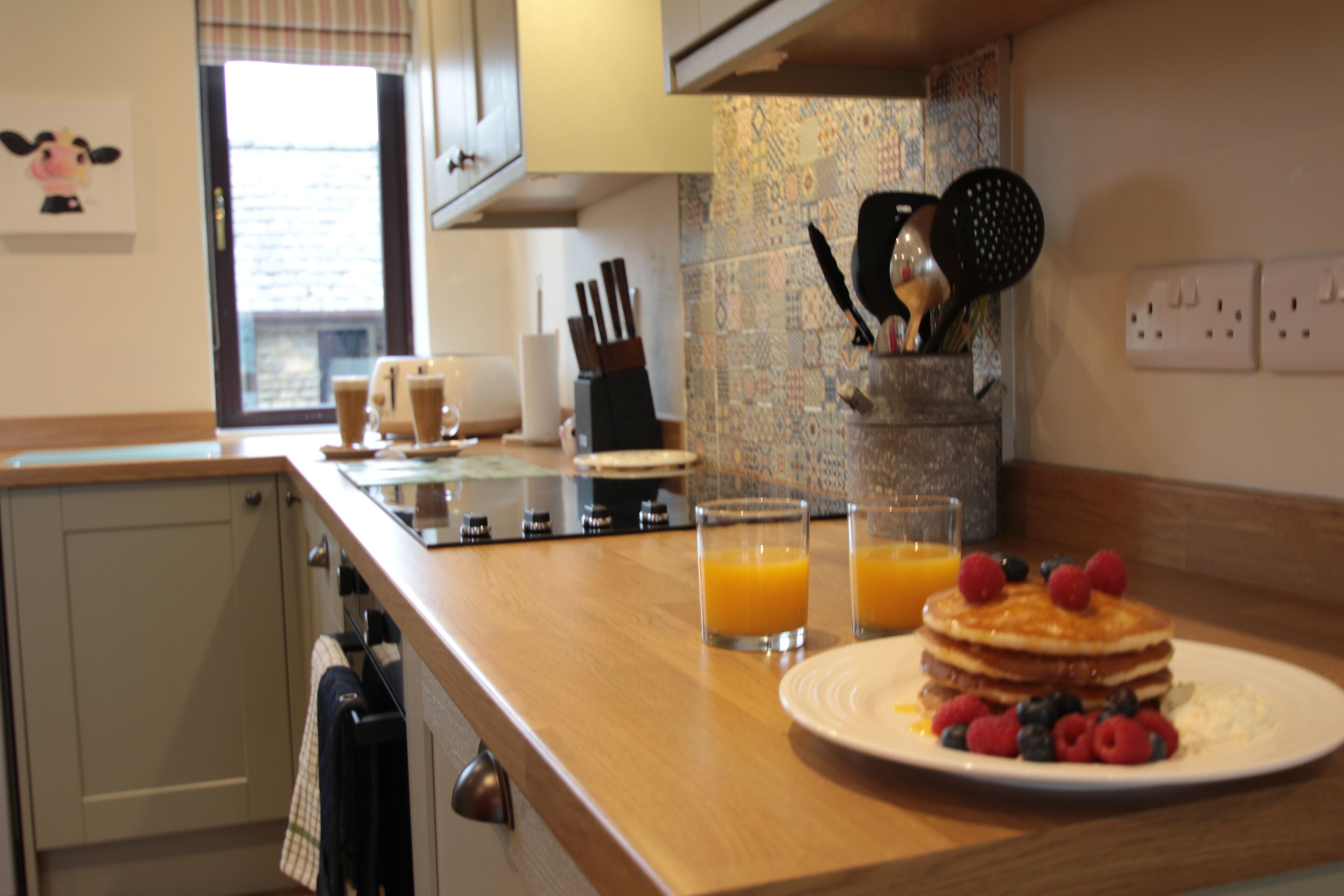 Une cuisine avec une assiette de crêpes, des fruits rouges et des verres de jus d’orange, prêts pour le petit-déjeuner.