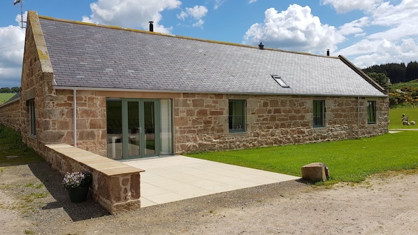 A stone building with a sloped roof, large glass doors, and a small garden area.