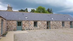 A stone building with a grey tiled roof, multiple windows, and a gravel driveway.
