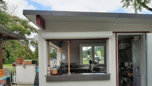 A small outdoor café with a counter, a window, and a door leading to a kitchen area. - Camping Uhaitza - Chalets (Gotein-Libarrenx)