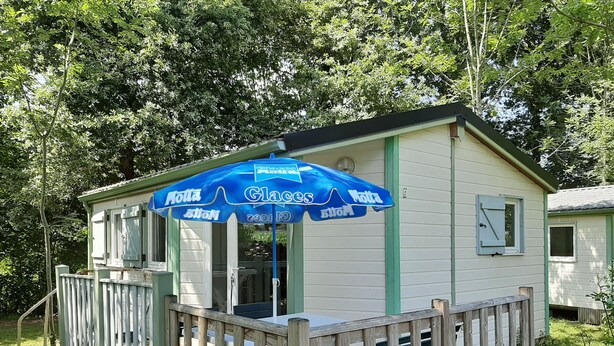 A small, single-story building with a covered porch and a blue umbrella. - Camping Uhaitza - Chalets (Gotein-Libarrenx)