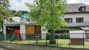 A residential building with a fenced yard, a red slide, and a covered play area. - Camping Uhaitza - Chalets (Gotein-Libarrenx)