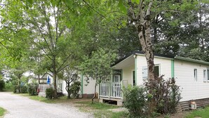 A row of single-story cabins with front porches, surrounded by trees and a gravel path. - Camping Uhaitza - Chalets (Gotein-Libarrenx)