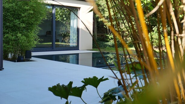 A modern building with large glass windows, a rooftop terrace, and a pond.