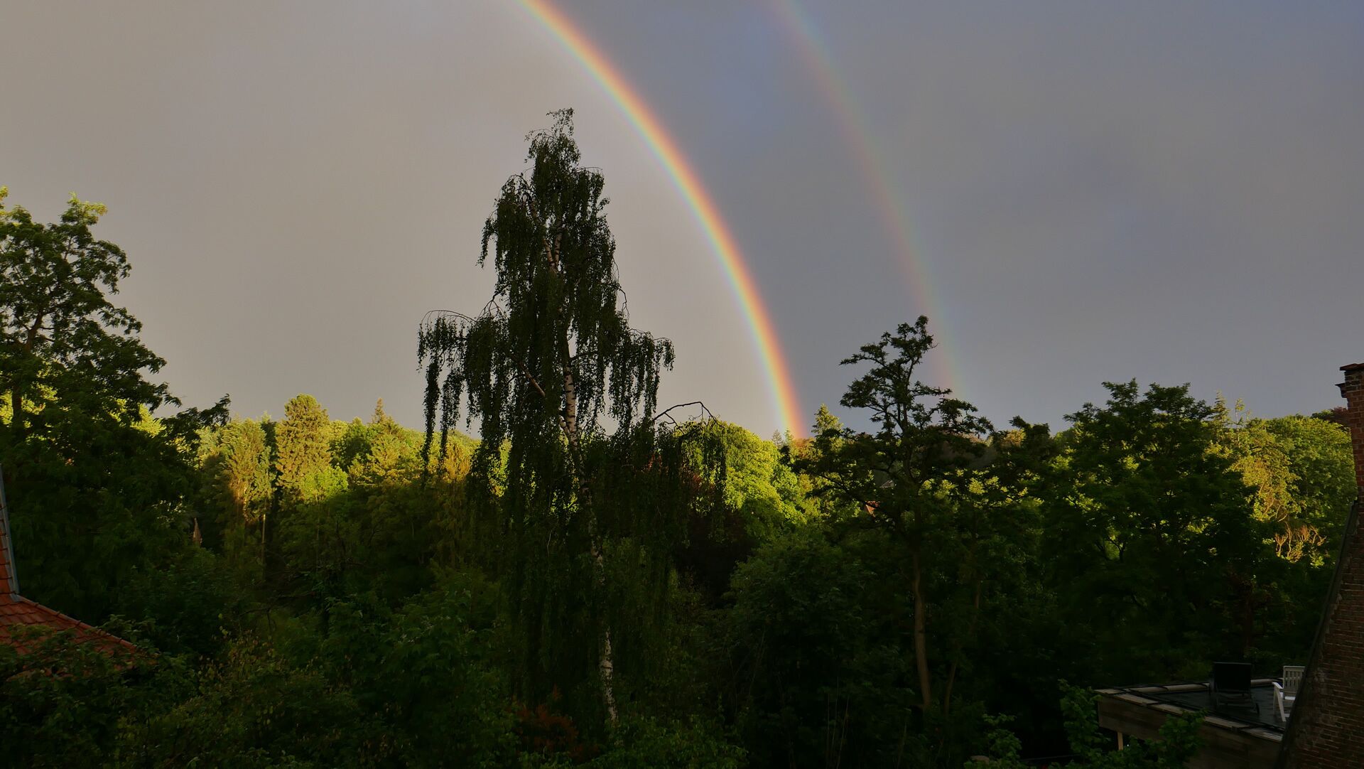 Une maison avec un jardin et un arc-en-ciel en arrière-plan.