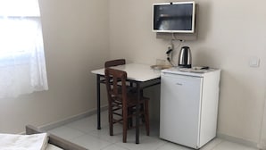 Una habitación pequeña y limpia con cama, escritorio, silla, televisor y refrigerador.