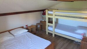 Quarto tipo dormitório com duas beliches, uma mesinha de cabeceira de madeira, uma pequena mesa e um lustre.