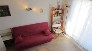 Um sofá vermelho, uma mesa de centro de madeira e um abajur em um quarto com piso de madeira clara e paredes brancas.