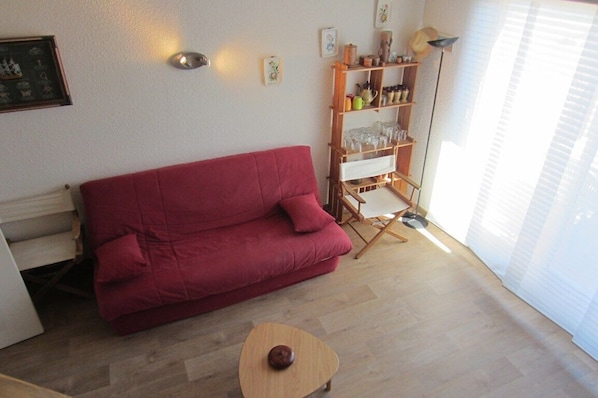 A red sofa, a wooden coffee table, and a floor lamp in a room with light wooden flooring and white walls.