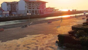 Uma praia com um edifício ao fundo, um calçadão e um pôr do sol.