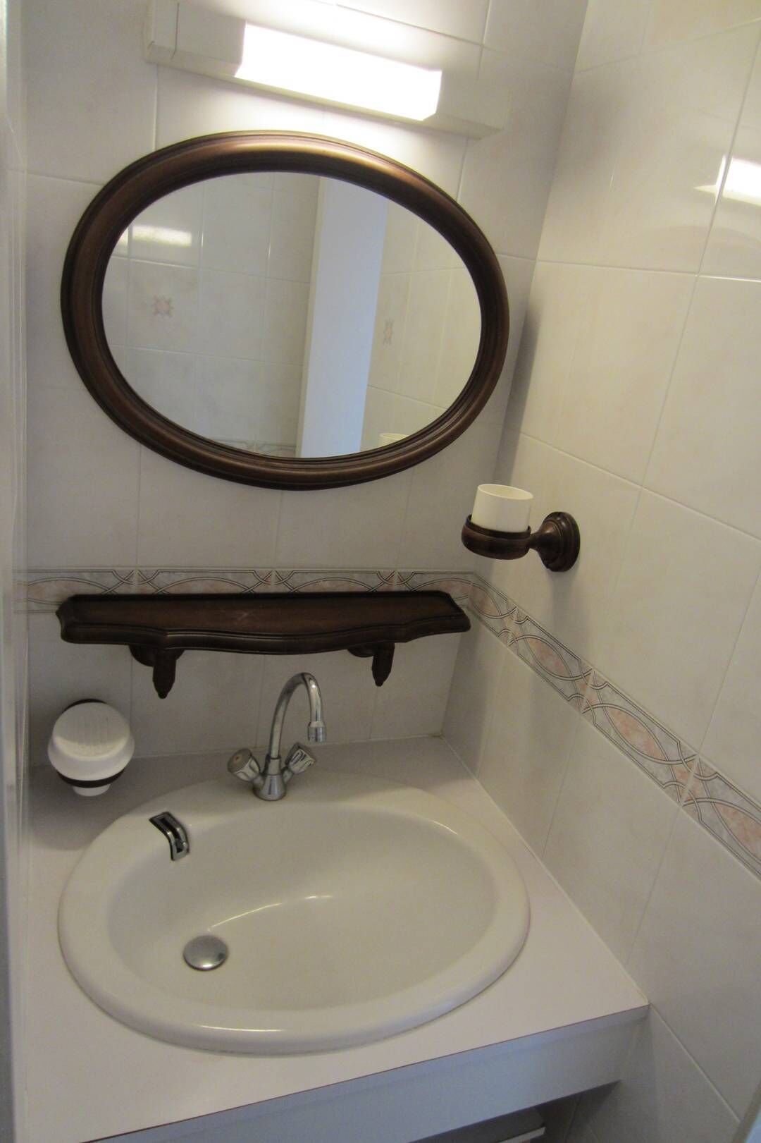 A bathroom with a round mirror, a white sink, a cup holder, and a decorative tile backsplash.