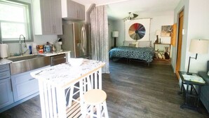 A compact kitchen with a bar stool, a bed with a patterned bedspread, and a decorative fan. - WanderLost WanderLoft - Ideal for ATU grad student, visiting faculty, ANO outage (Dover)