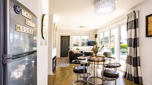 Une cuisine moderne dotée d’un réfrigérateur en acier inoxydable, d’un coin repas avec une table ronde et des tabourets de bar, et d’une grande fenêtre offrant une vue sur l’extérieur.