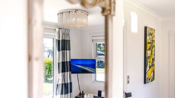 A room with a television mounted on the wall, a chandelier, a striped curtain, and a painting.
