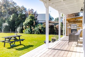 Un patio couvert avec un barbecue, des sièges d’extérieur et une table de pique-nique.