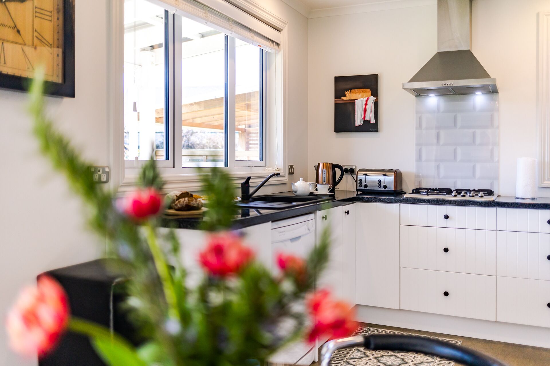 A modern kitchen with white cabinets, a stainless steel range hood, and a window with blinds.