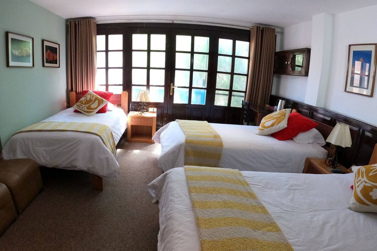 A hotel room with two beds, a brown leather armchair, a wooden nightstand, and a window with curtains.