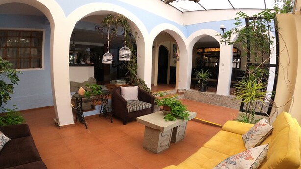 Amplio espacio interior con una zona de estar, que incluye un sofá y sillones, una mesa de piedra con plantas y jaulas de pájaros colgantes.