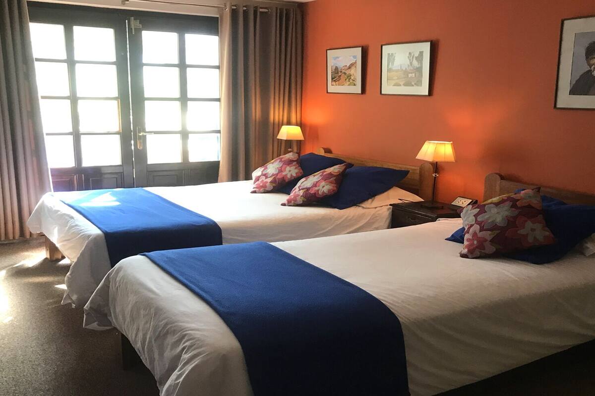 A hotel room with two beds, each with blue bedding and floral pillows. There are two wall-mounted lamps on either side of the beds.