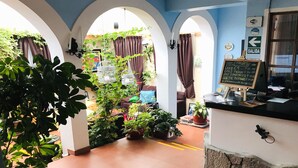 Un interior acogedor con arcos, plantas en macetas, un menú en pizarra y vistas al exterior.
