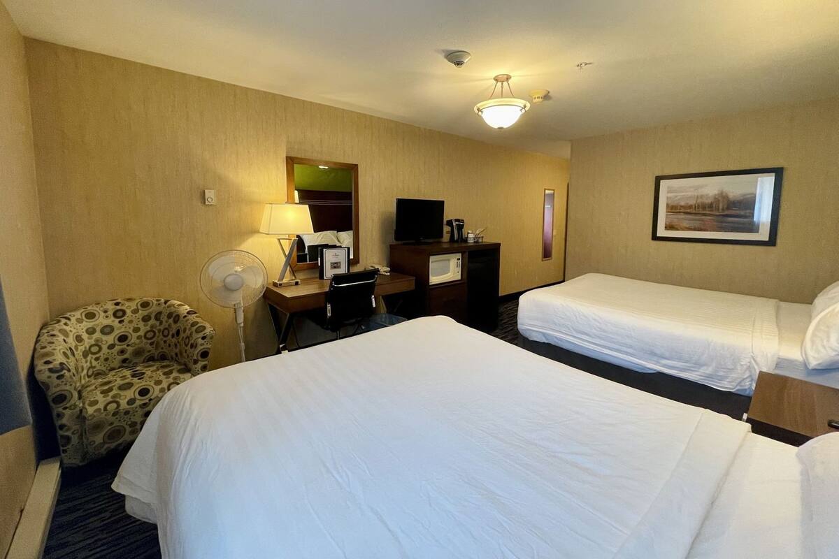 Ein Hotelzimmer mit zwei Betten, einem Schreibtisch mit Computer, einem Stuhl, einem Ventilator und einem Bild an der Wand.