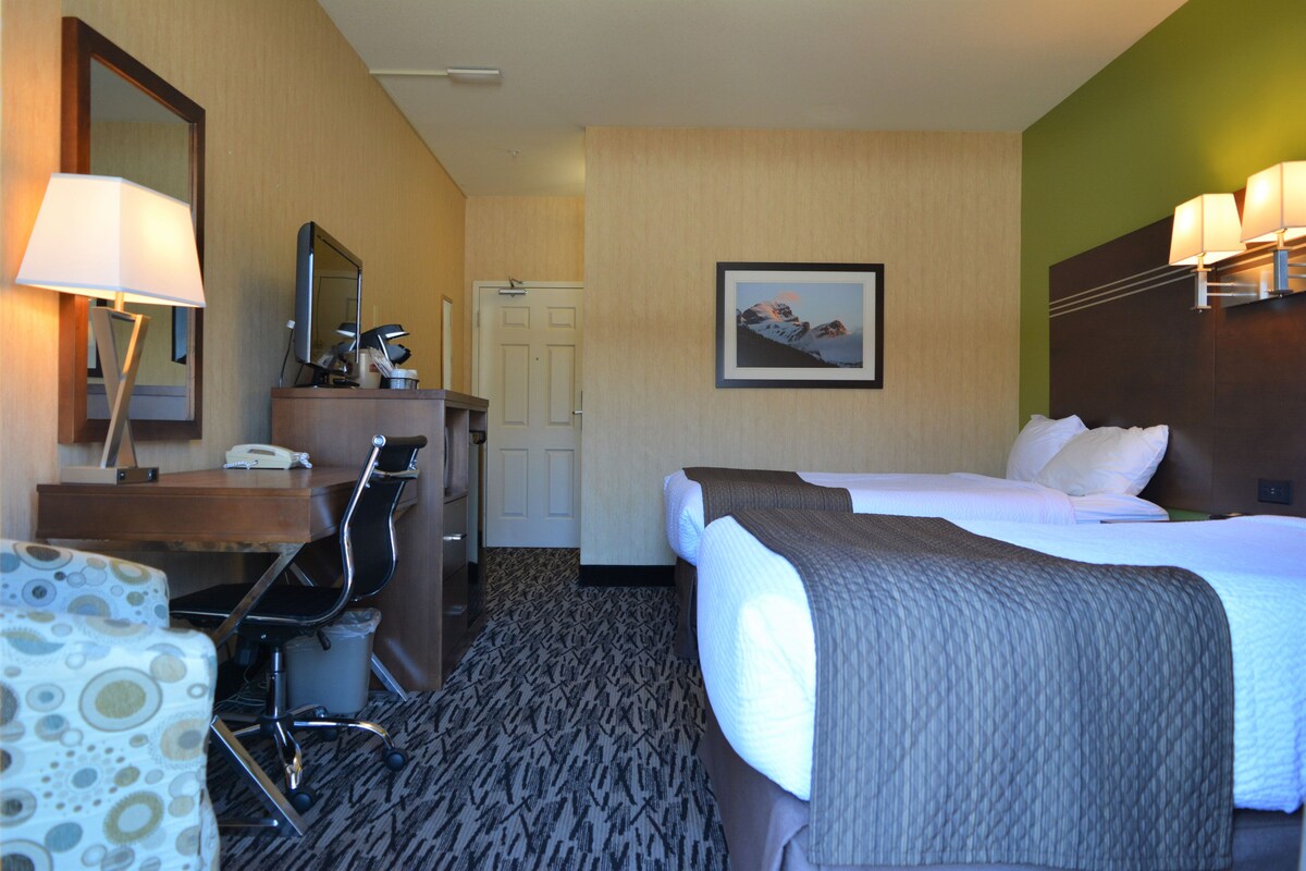 A hotel room with a bed, desk, chair, and a mirror.